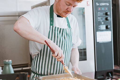Man wearing an apron preparing food in a metal dish